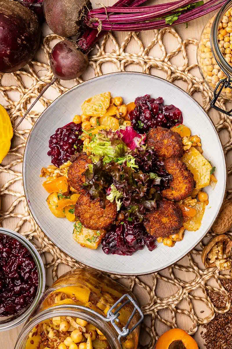 Gemüsegratin mit knusprigen Linsentalern, frischem Salat, Kichererbsen und Rotkohl, dekoriert mit saisonalen Zutaten.