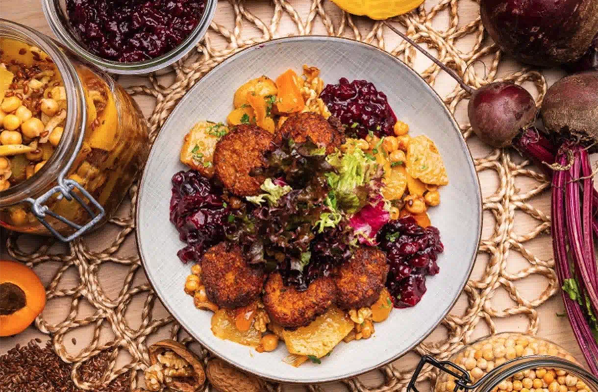 Gemüsegratin mit knusprigen Linsentalern, frischem Salat, Kichererbsen und Rotkohl, dekoriert mit saisonalen Zutaten.