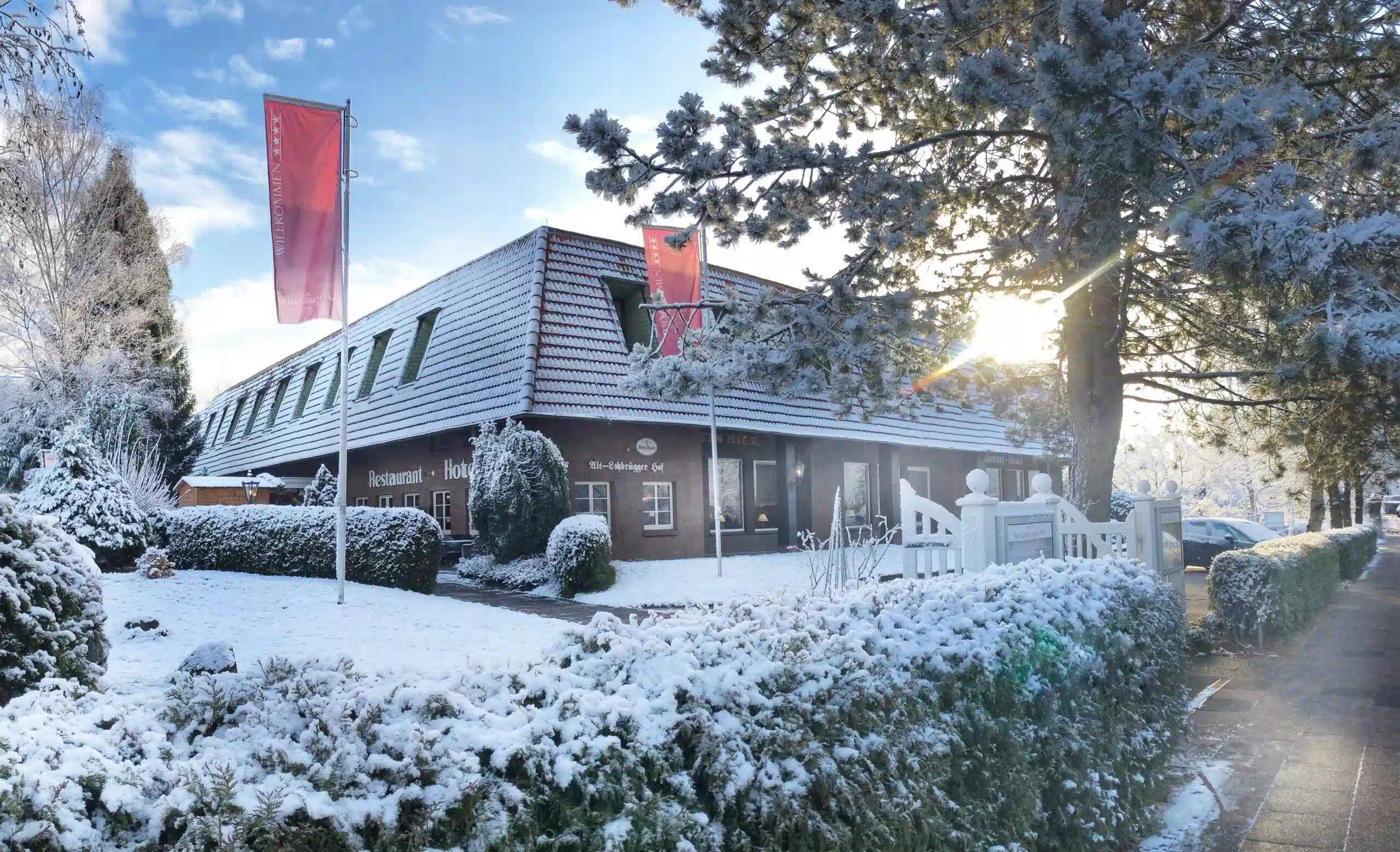 Außenansicht des schneebedeckten Hoteleingangs vom Alt Lohbrügger Hof bei tief stehender Sonne