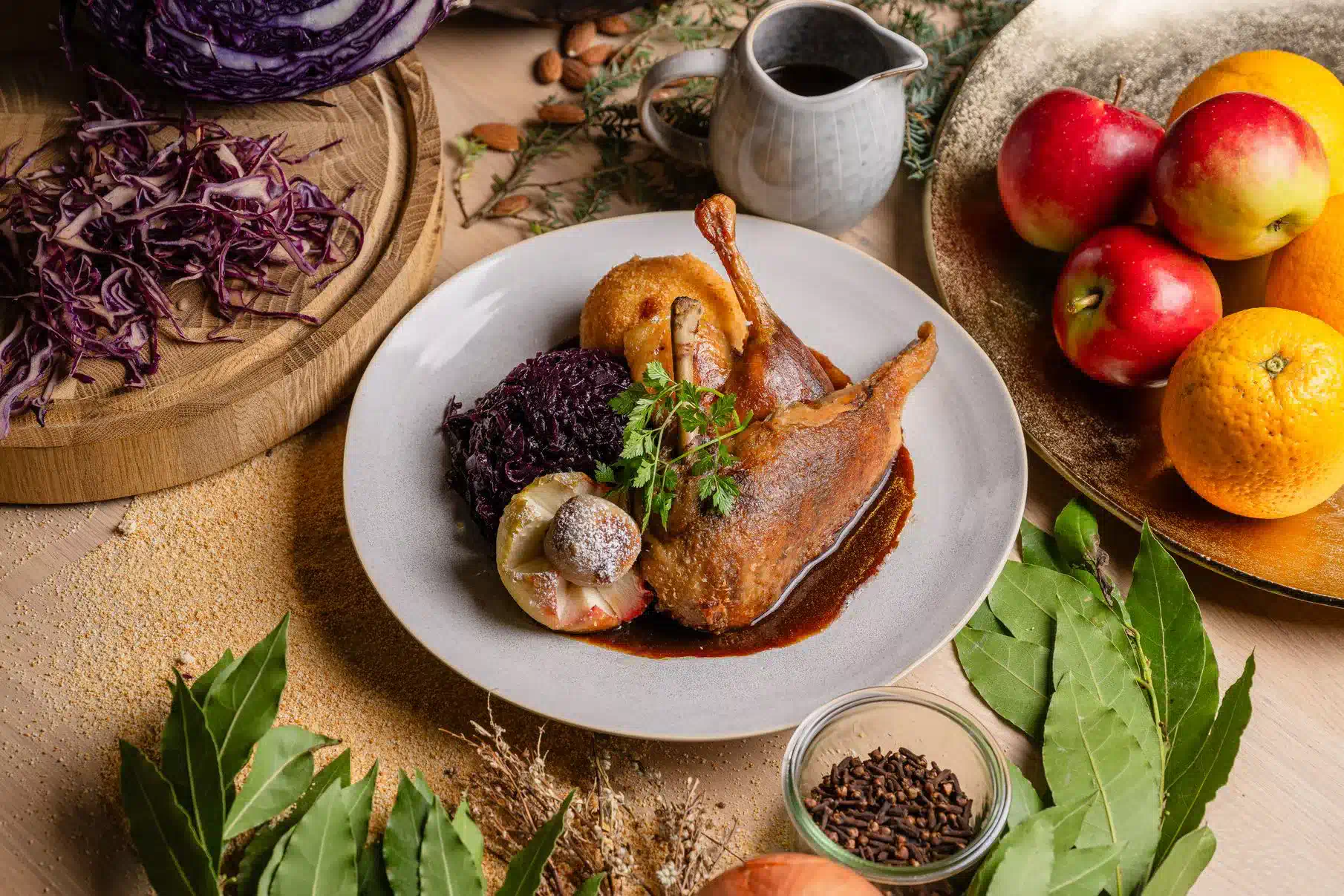 Brust und Keule von der Ente mit Rotkohl, Kartoffelkloß und Bratapfel auf einem winterlich dekorierten Tisch