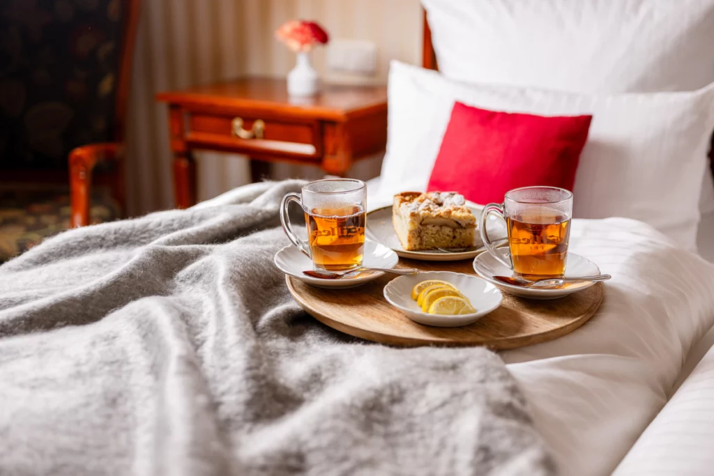 Schwarzer Tee mit Zitrone und einem Stück Küchen, angerichtet auf einem runden Holztablett auf dem Bett